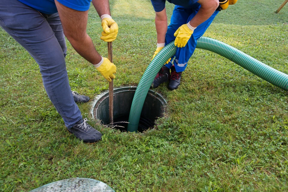 Deux techniciens en tenue de travail effectuent une intervention d'assainissement sur une fosse septique dans un jardin résidentiel