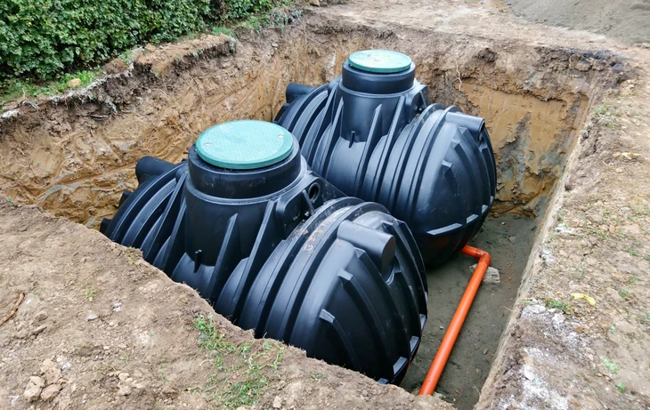 Deux ouvriers en casques orange travaillent à genoux sur un chantier de terrassement, manipulant des canalisations bleues