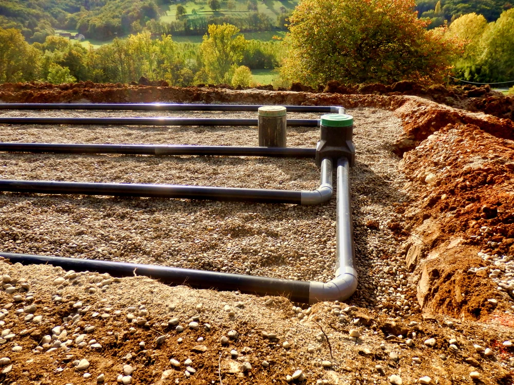 Scène extérieure sur terrain de terre, mains d'ouvrier en gants de protection gris manipulant un outil de serrage sur raccordement de canalisation